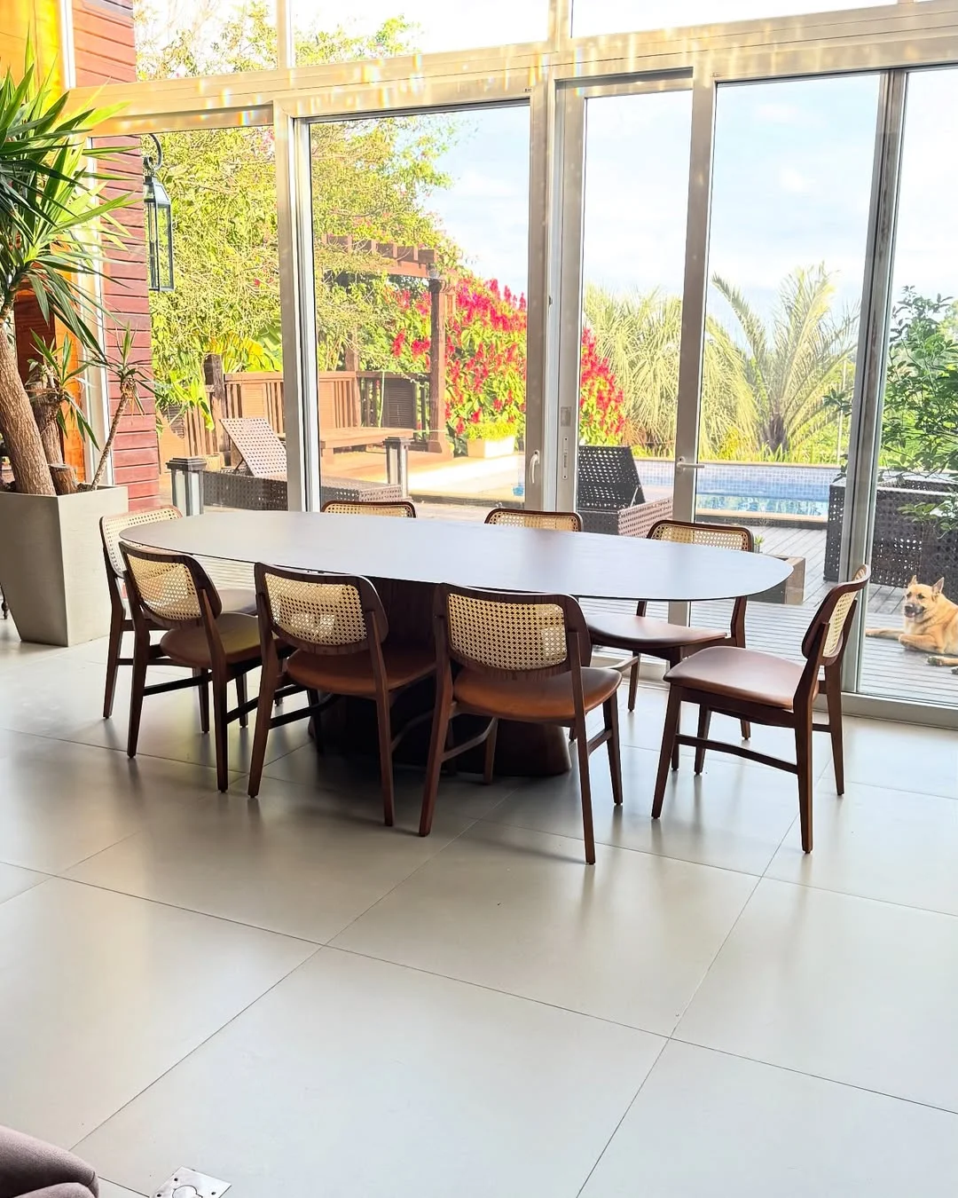Mesa de jantar oval com cadeiras de palhinha e vista para a piscina